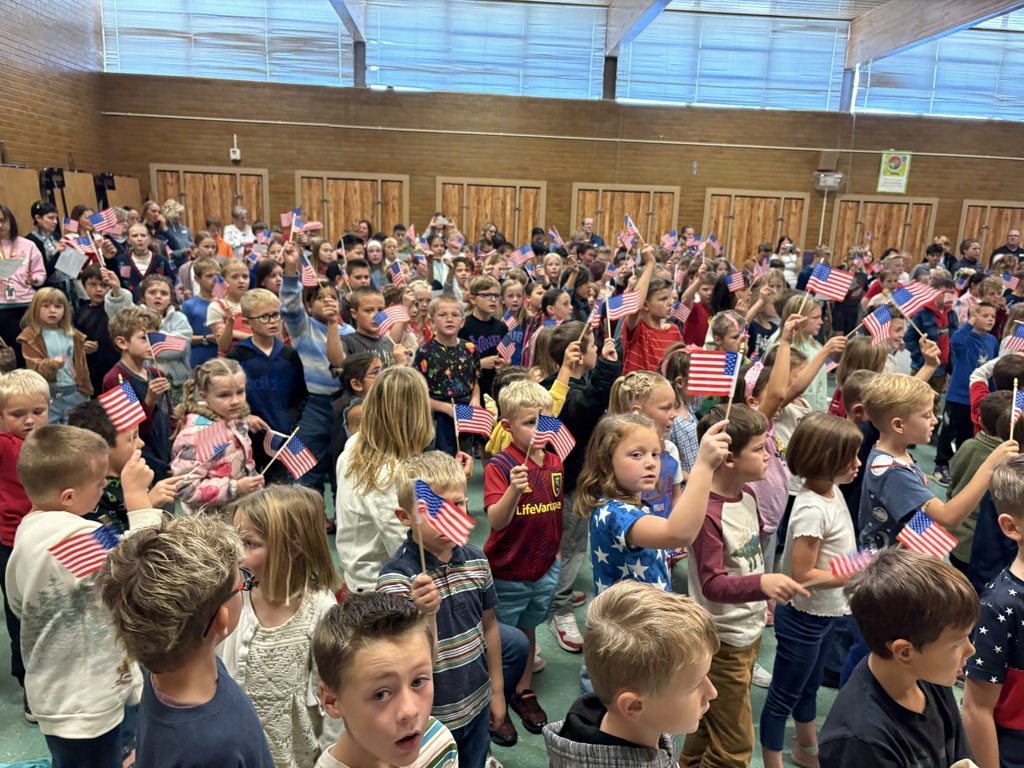 Image of students waving flags and signing at Veterans Day Assembly