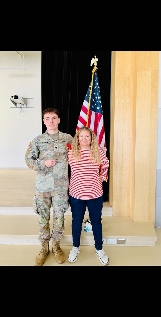 Mr Zach, dressed in his military uniform, and Ms Baron, his mom, our own Doxey employees pose together in front of the flag.