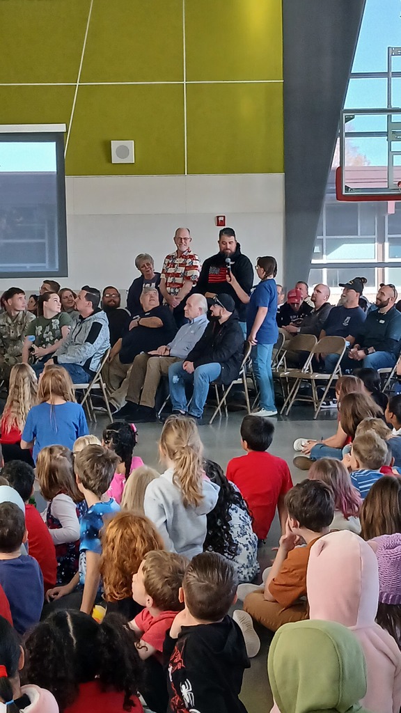 1 student stands next to her 3 family members as they stand to be introduced by her and share how long they served and in what branch.