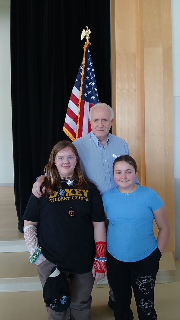 2 girl students posing in front of their older male relative veteran.