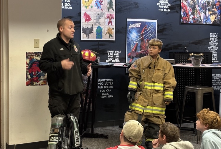 5th grader trying on fireman’s uniform during demonstration