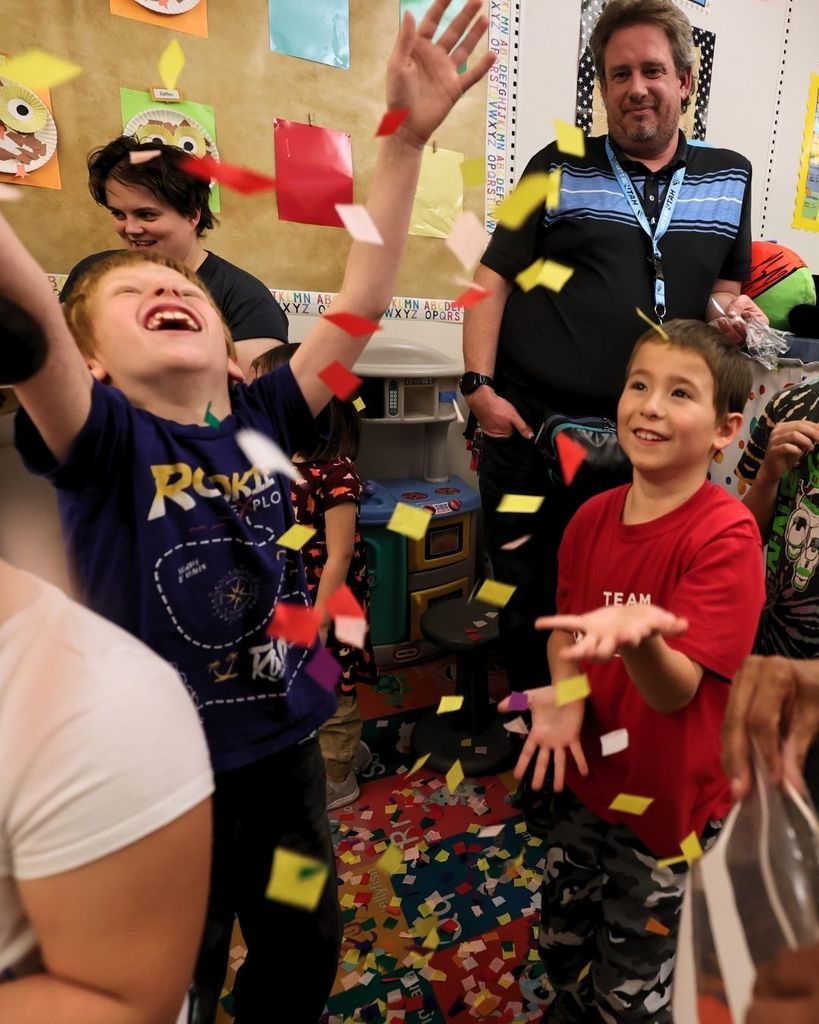 Students in a classroom smiling and catching confetti. 