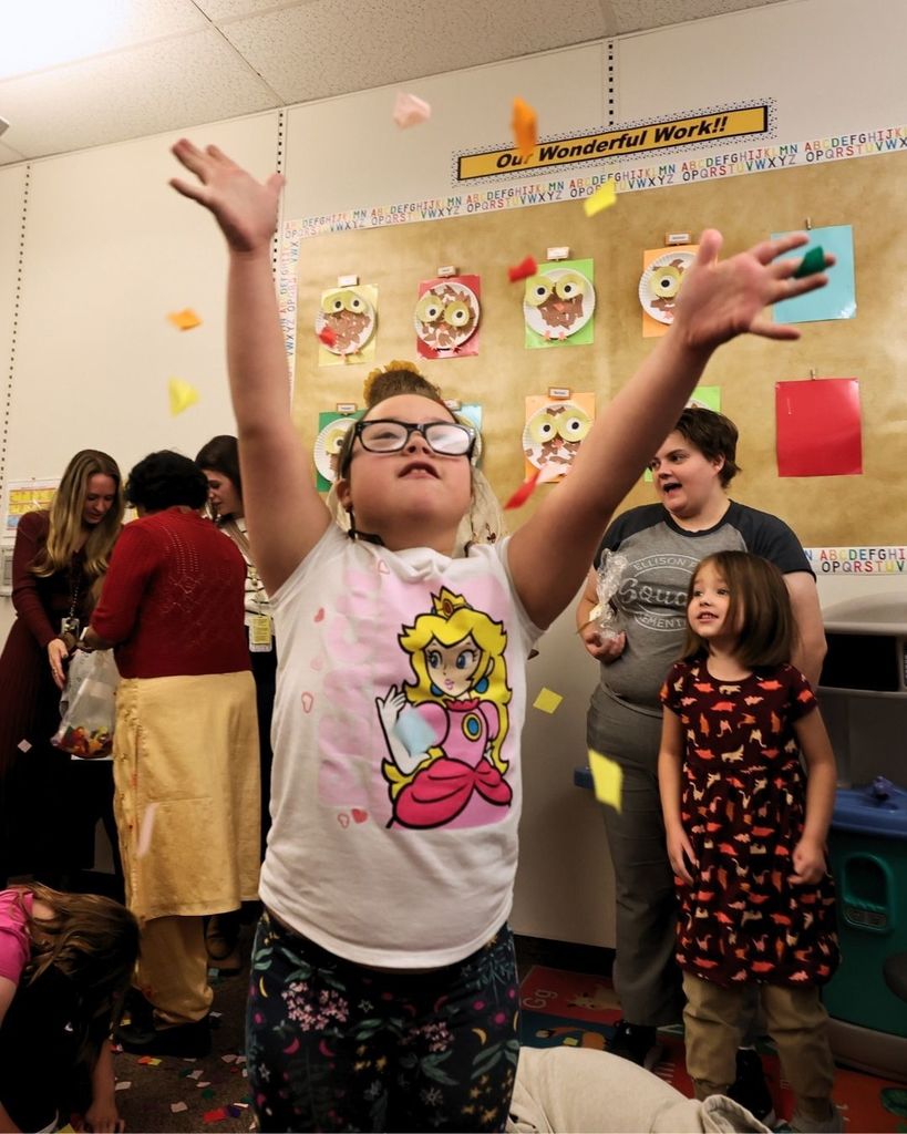 Students in a classroom smiling and catching confetti. 