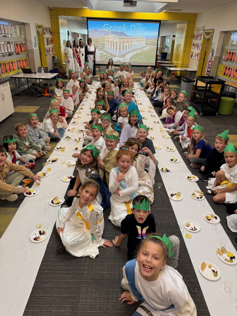 students dressed in Greek attire seated on the floor trying Greek foods
