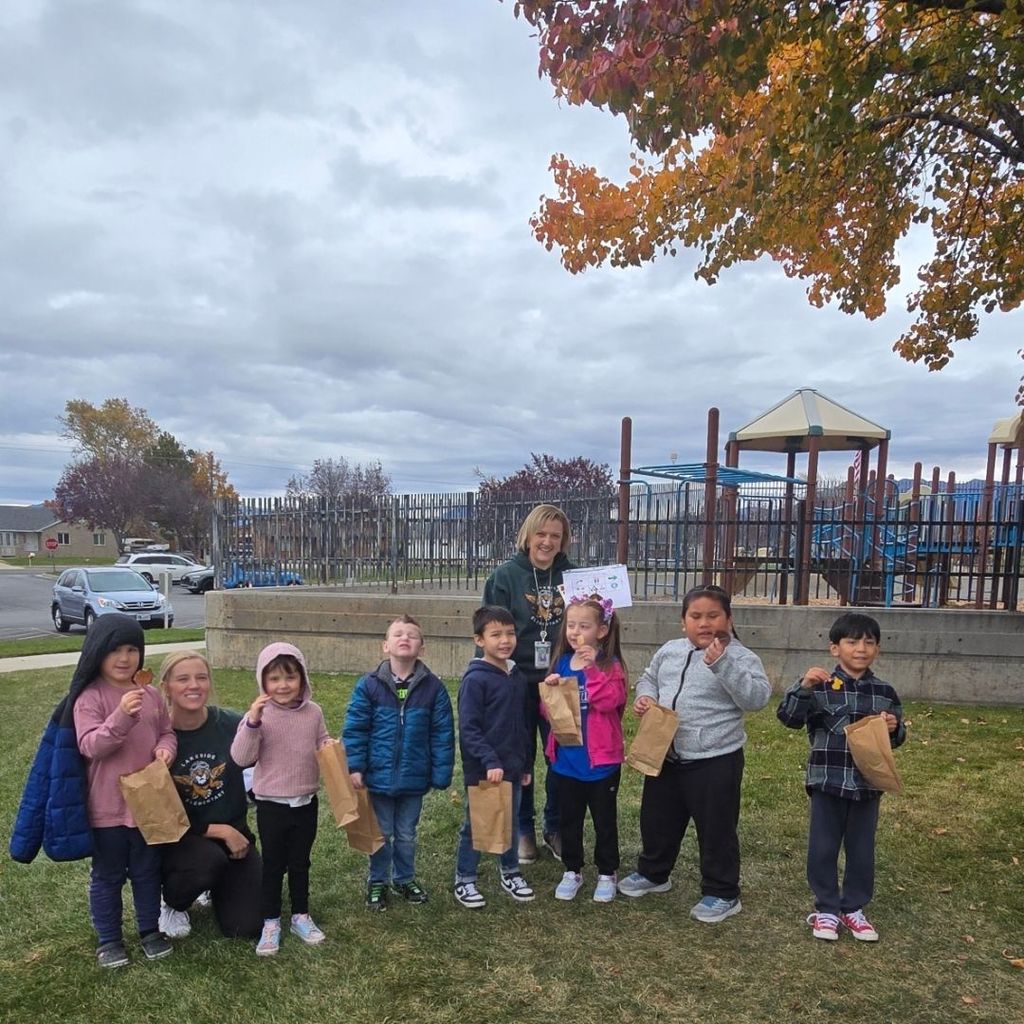 Students and teachers pose for a picture outside holding leaves.