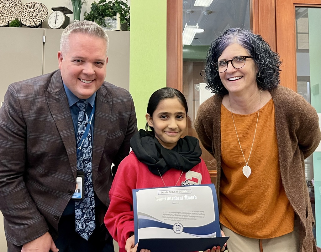A 5th grade female student holding a certificate, standing in between her Elementary Principal and District Superintendent