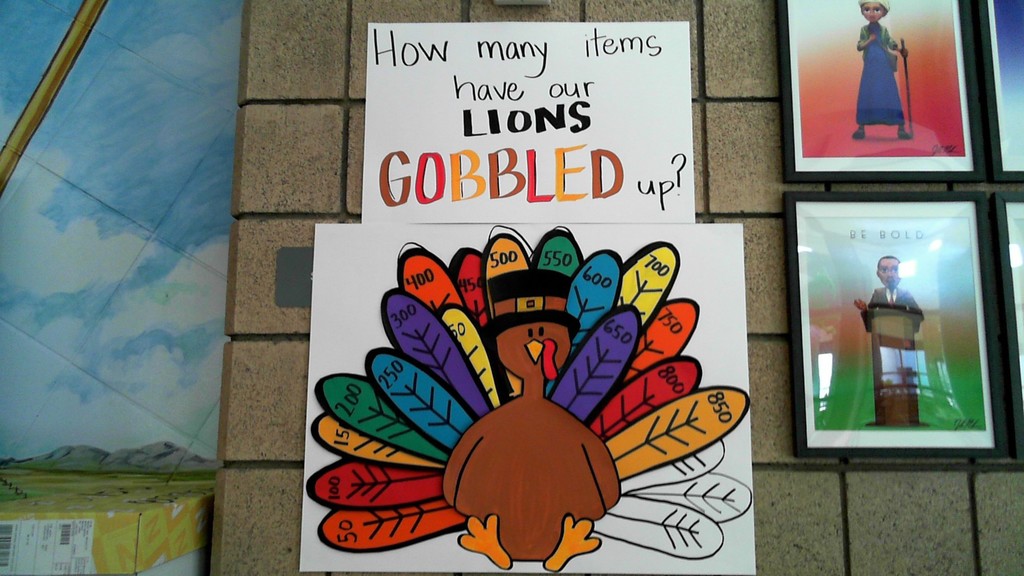 Picture of a turkey can count with colorful feathers for every 50 cans of donated food. Sign that says How Many items have our lions gobbled up? above the turkey.