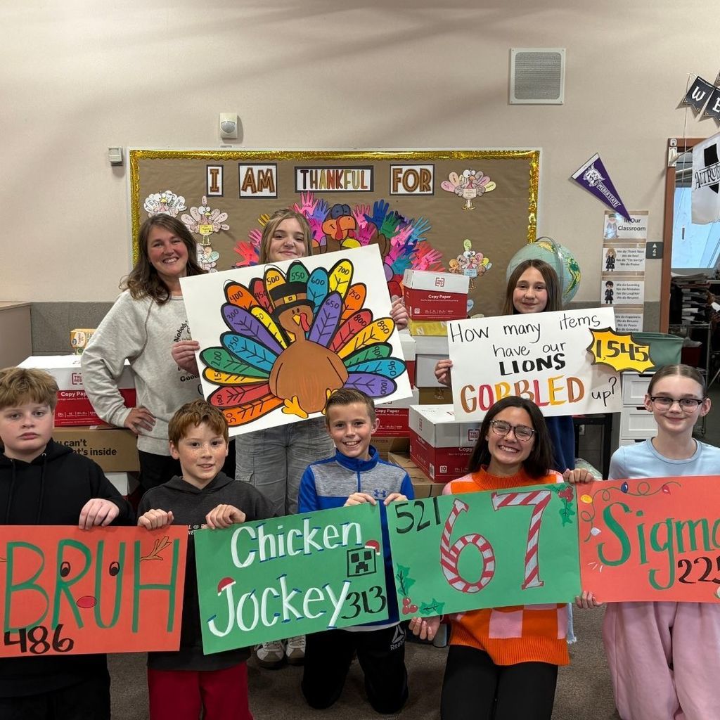 Students and a teacher holding signs for a Food drive.