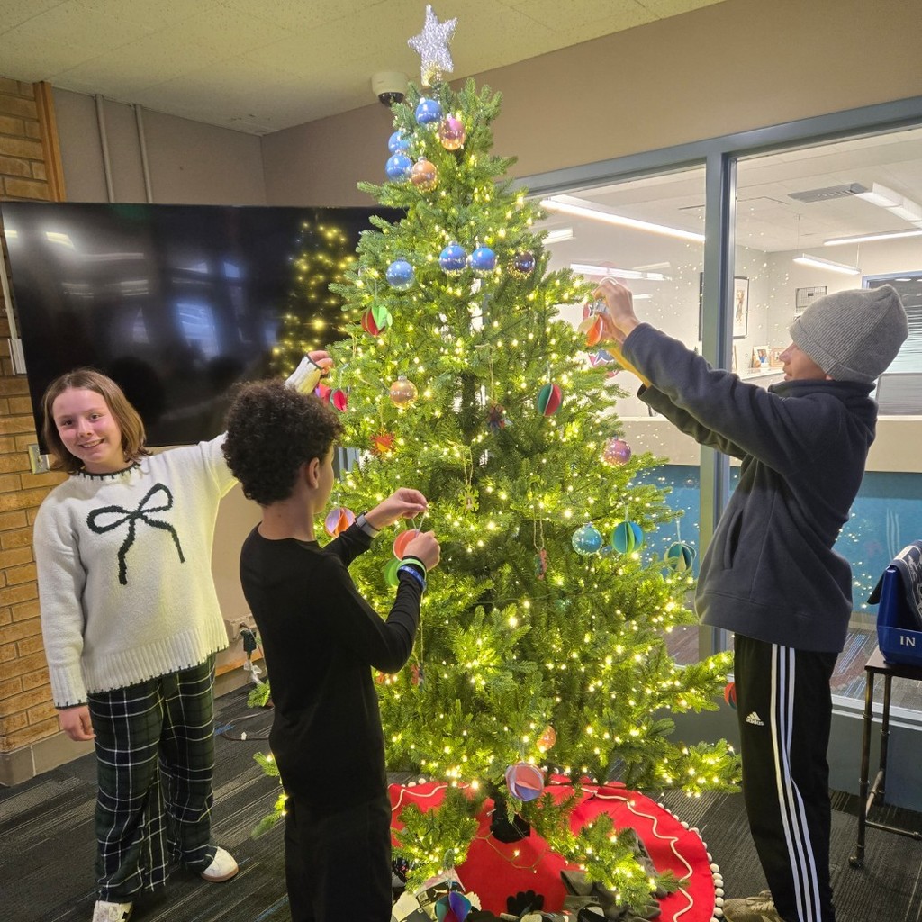three Meadowbrook students from 6th grade help decorate the Christmas tree in front of meadowbrooks office