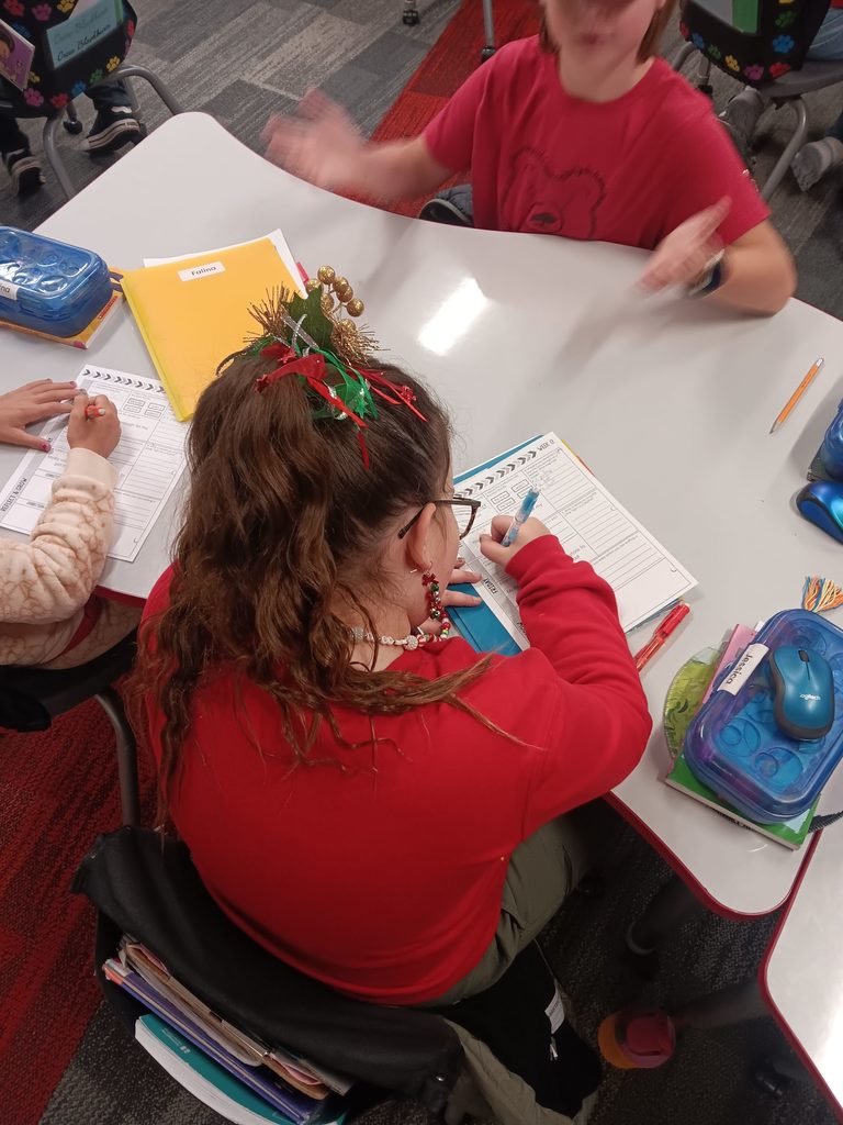 Back of a student wearing a red sweater with a glitter hair piece working on ELA. 