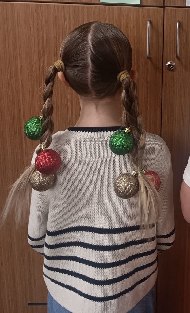 Back of a student with two braids in hair with Christmas ornaments attached to each braid. 