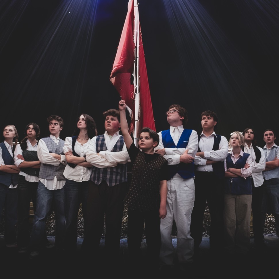 Army of students dressed in Les Mis costumes standing in front of a flag