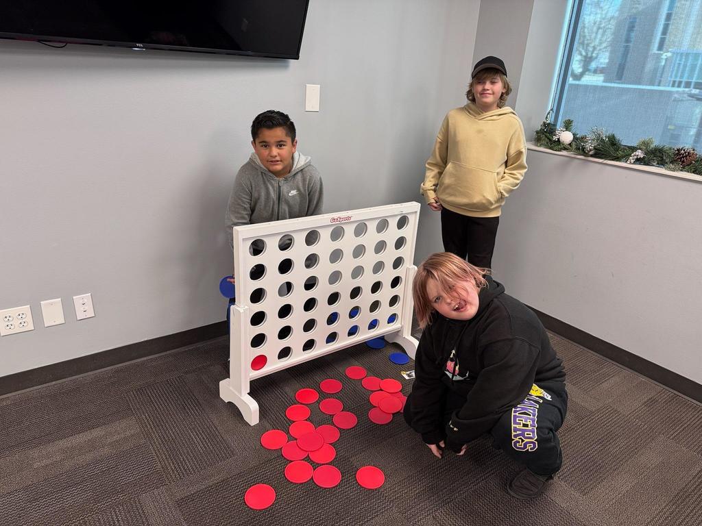 Three Doxey Elementary students playing a giant game of Connect 4 with red and blue pieces during their luncheon with Mayor Shepherd.