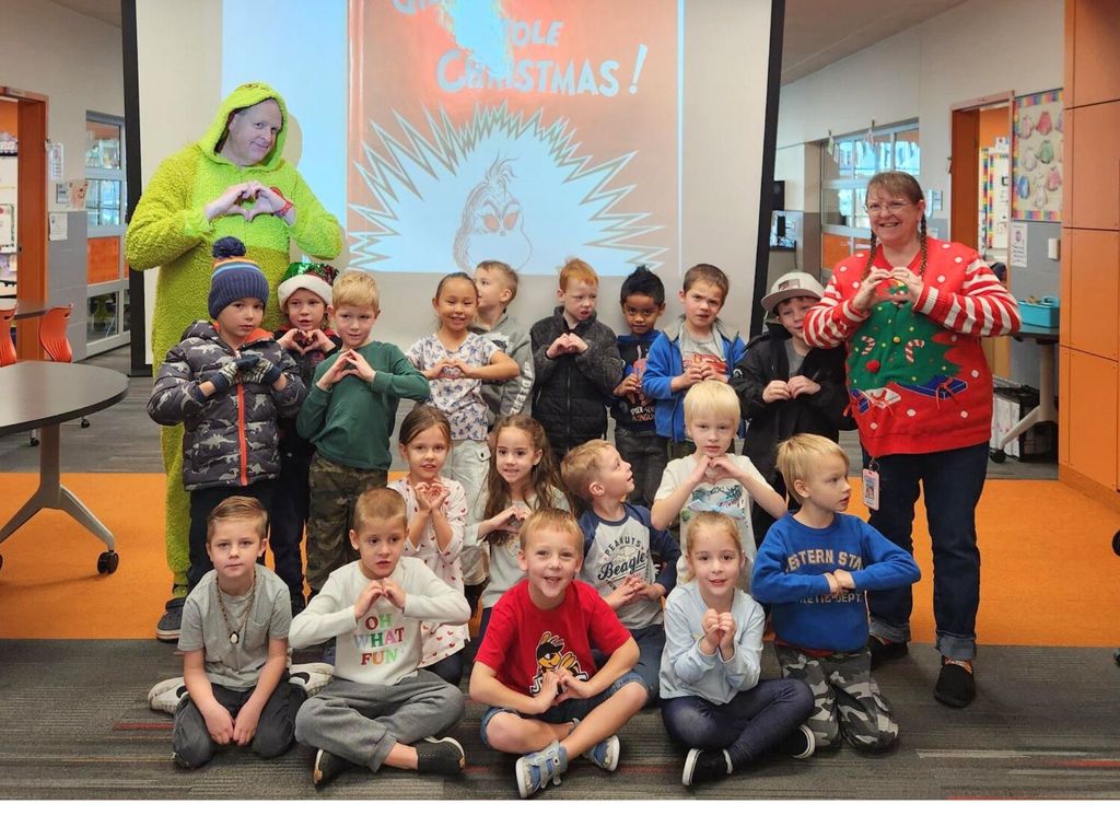 Elementary students pose together with staff members dressed as the Grinch and in holiday attire during a festive school activity.