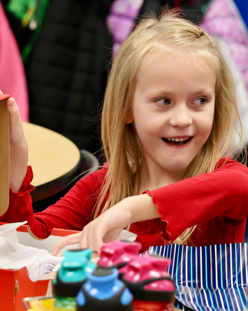 Kindergarten student smiles excitedly as she opens a new pair of shoes