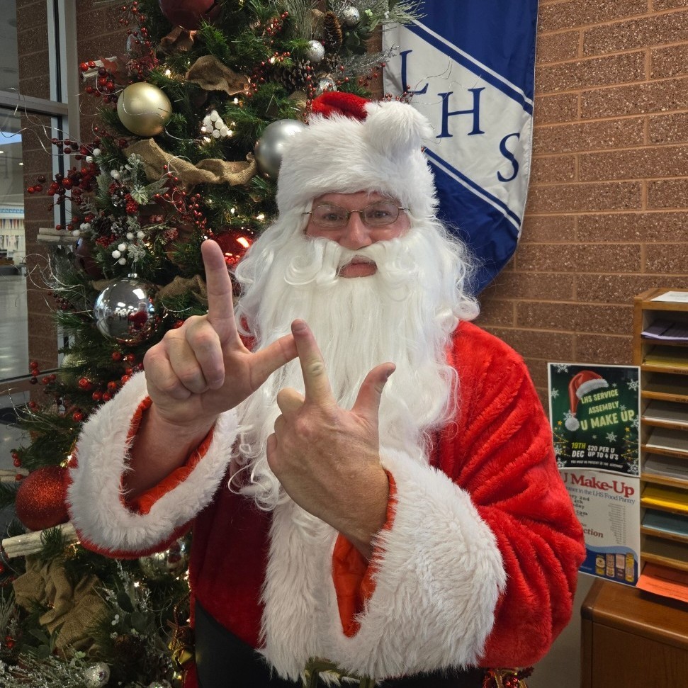 Santa doing the Double L with his hands for Layton Lancers standing in front of the office Christmas Tree