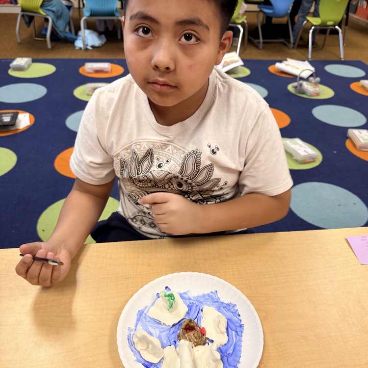 second grader painting their clay model of landforms and bodies of water