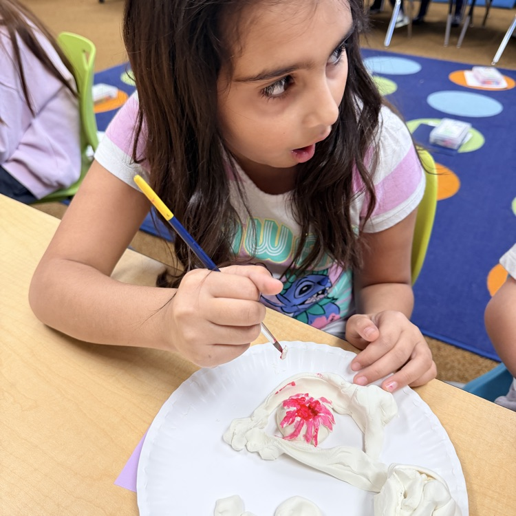 second grader painting their clay model of landforms and bodies of water