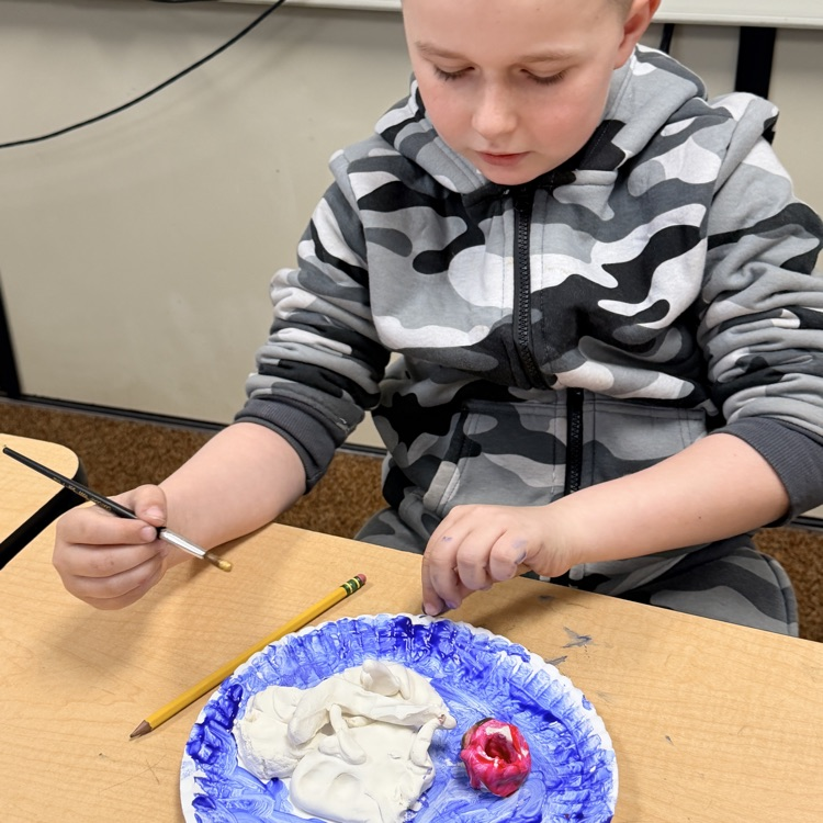 second grader painting their clay model of landforms and bodies of water