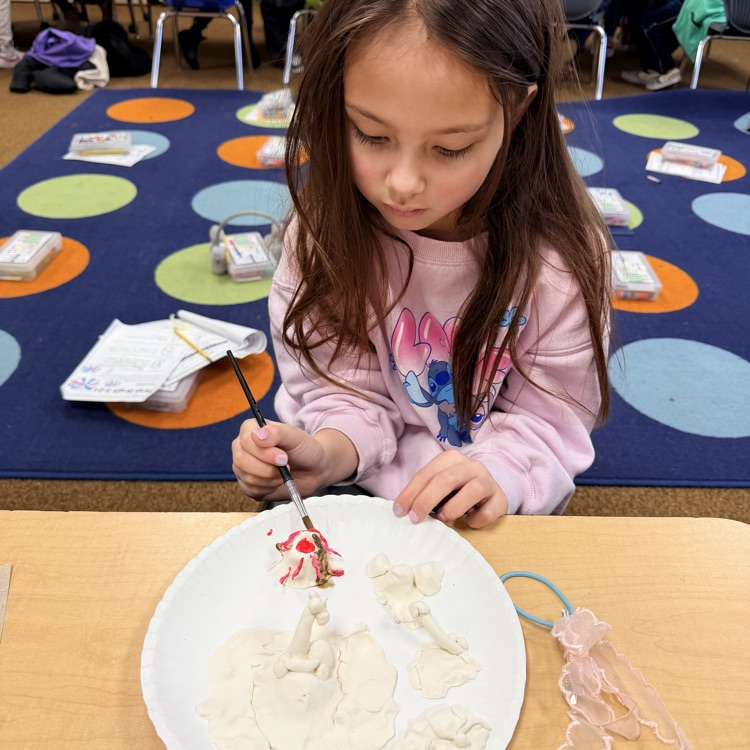 second grader painting their clay model of landforms and bodies of water