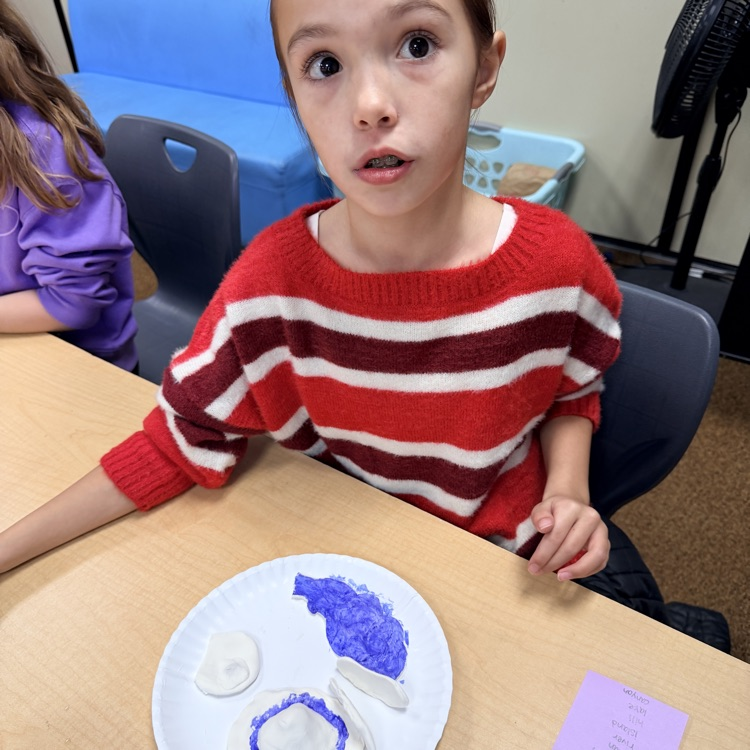 second grader painting their clay model of landforms and bodies of water