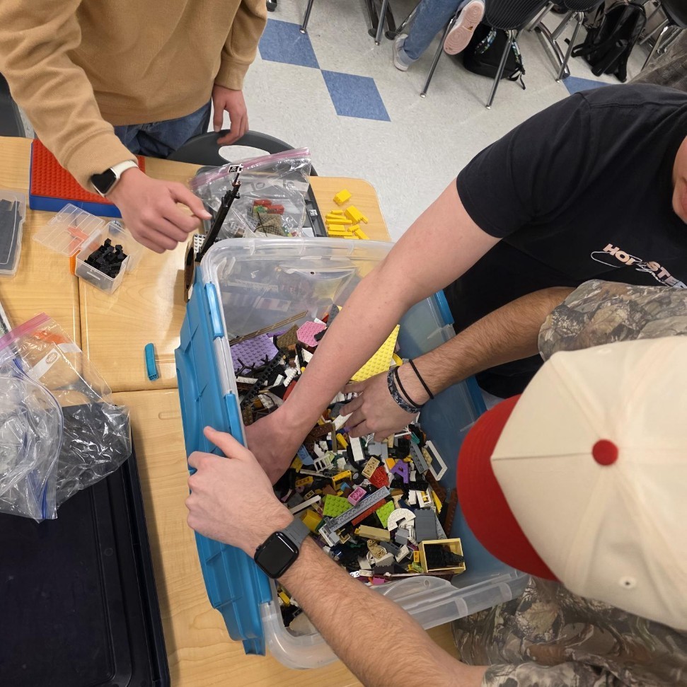 three students reaching into a bin of legos