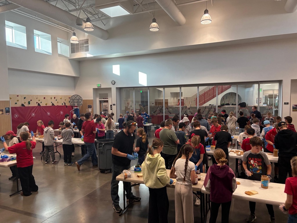 Students in the DEEP program working with volunteers to make pb&j sandwiches in the gym.