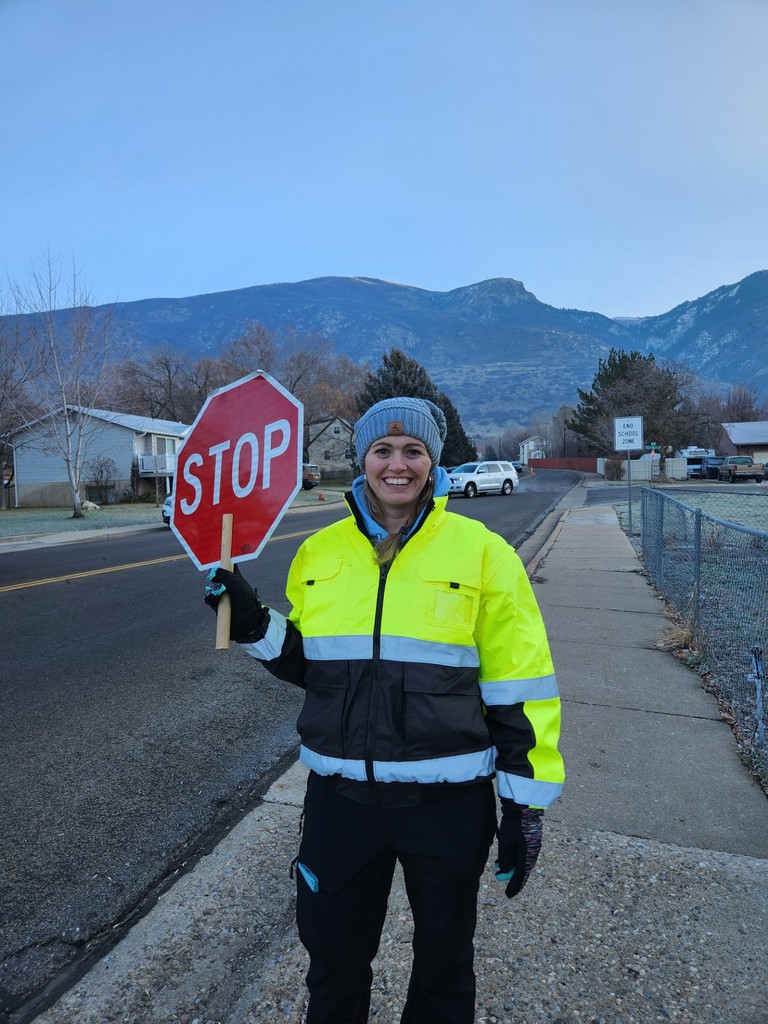 our crossing guard out in front of the school smiling and holding up a stop sign
