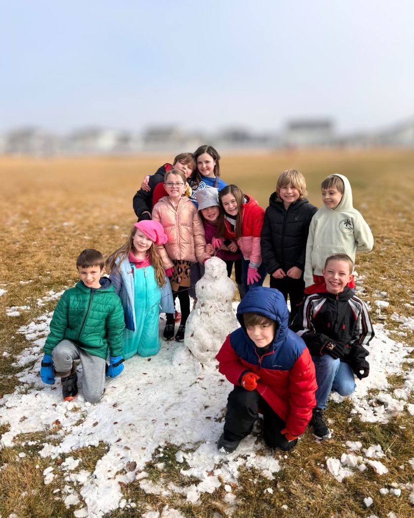 third grade students posing in front of their snowman at recess