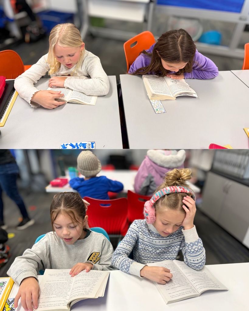 Two students sit side by side at desks reading books together during intervention time. Both students are focused on their reading.