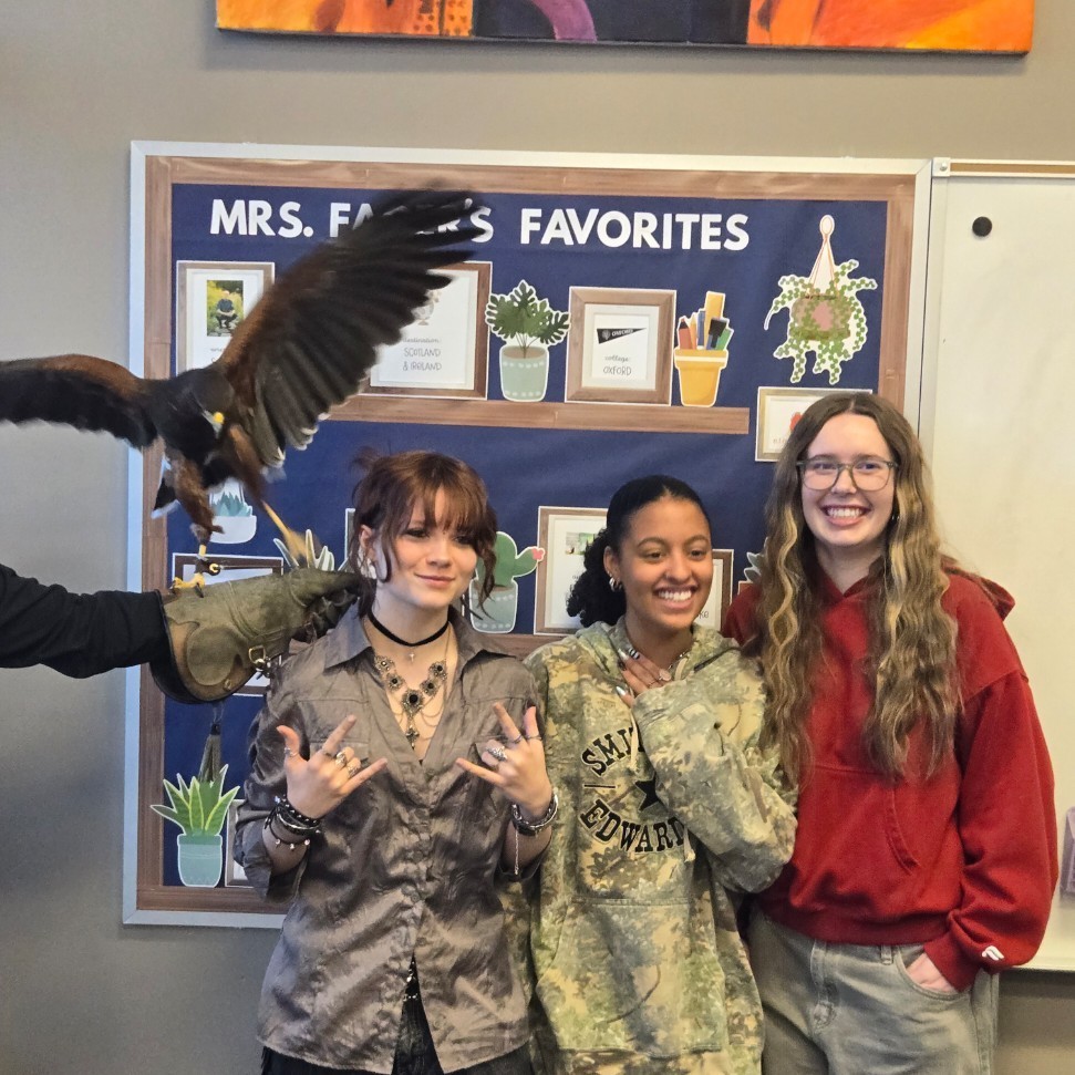 Three female students posing next to a harris hawk
