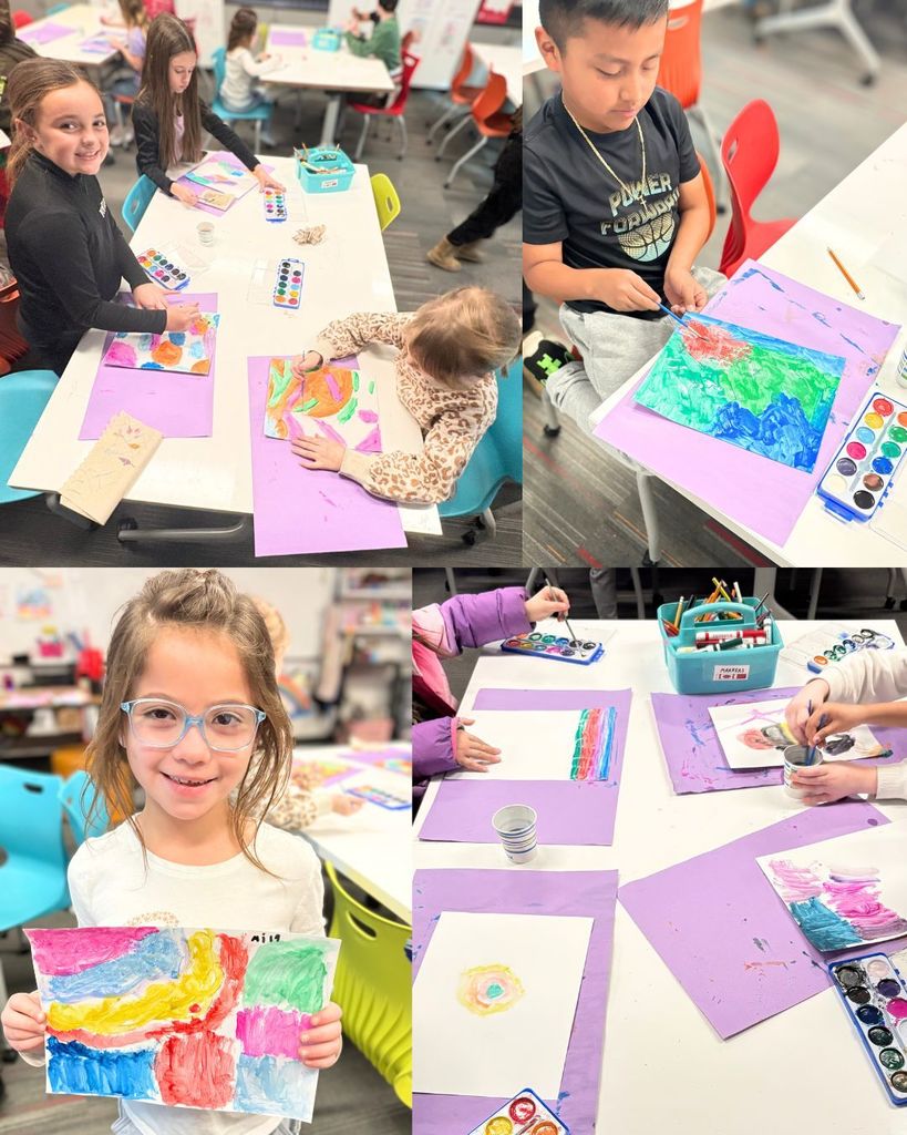 Young students sitting at tables in the art room painting colorful backgrounds with watercolors. One student smiles while holding up a finished abstract painting.