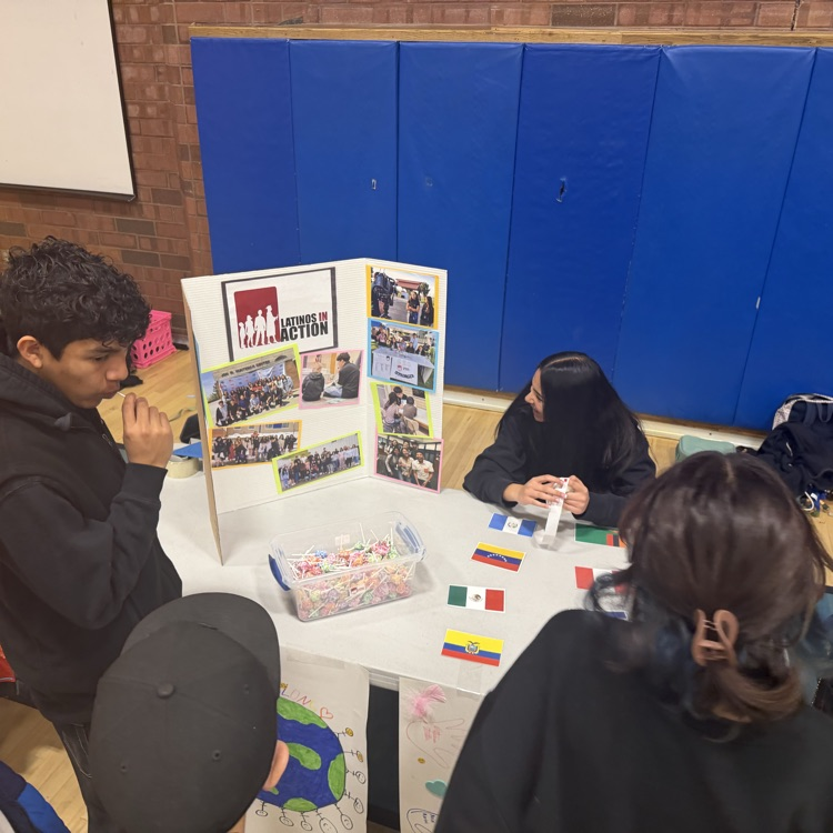 Latinos In Action club officers sit at a table presenting information about the LIA club to future 7th graders