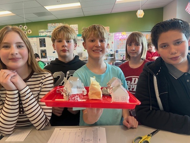 5 students holding a tray with paper houses on it