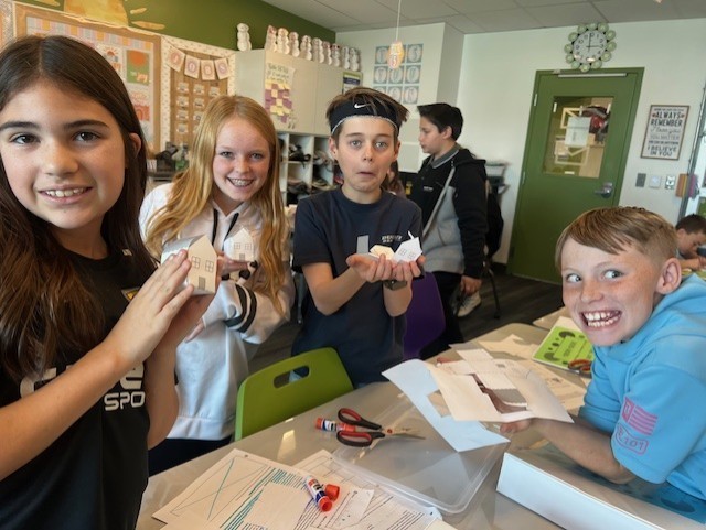 four students smiling whiling holding paper houses in their hands
