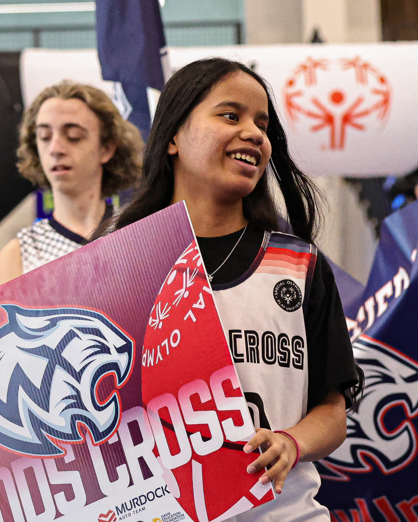 A Woods Cross Student smiles as they hold a Woods Cross Special Olympics sign.