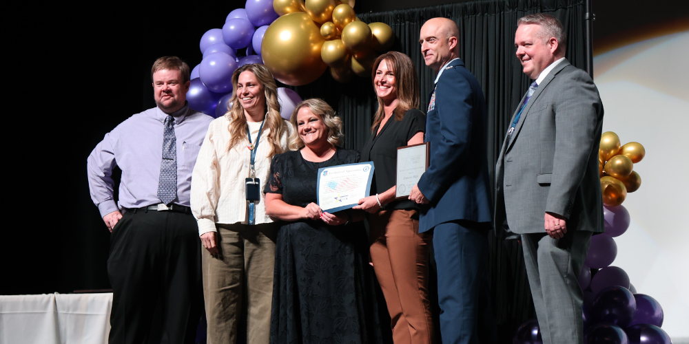 District and School personnel posing in front of purple and gold balloons for a purple star school presentation. 