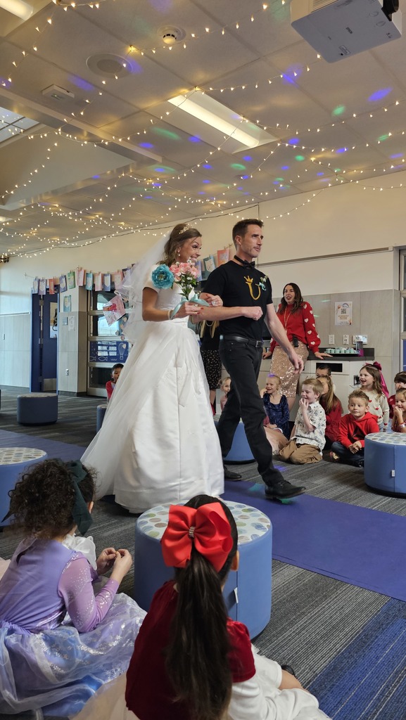 man with U on shirt and women in brides down walking down middle of room with students around