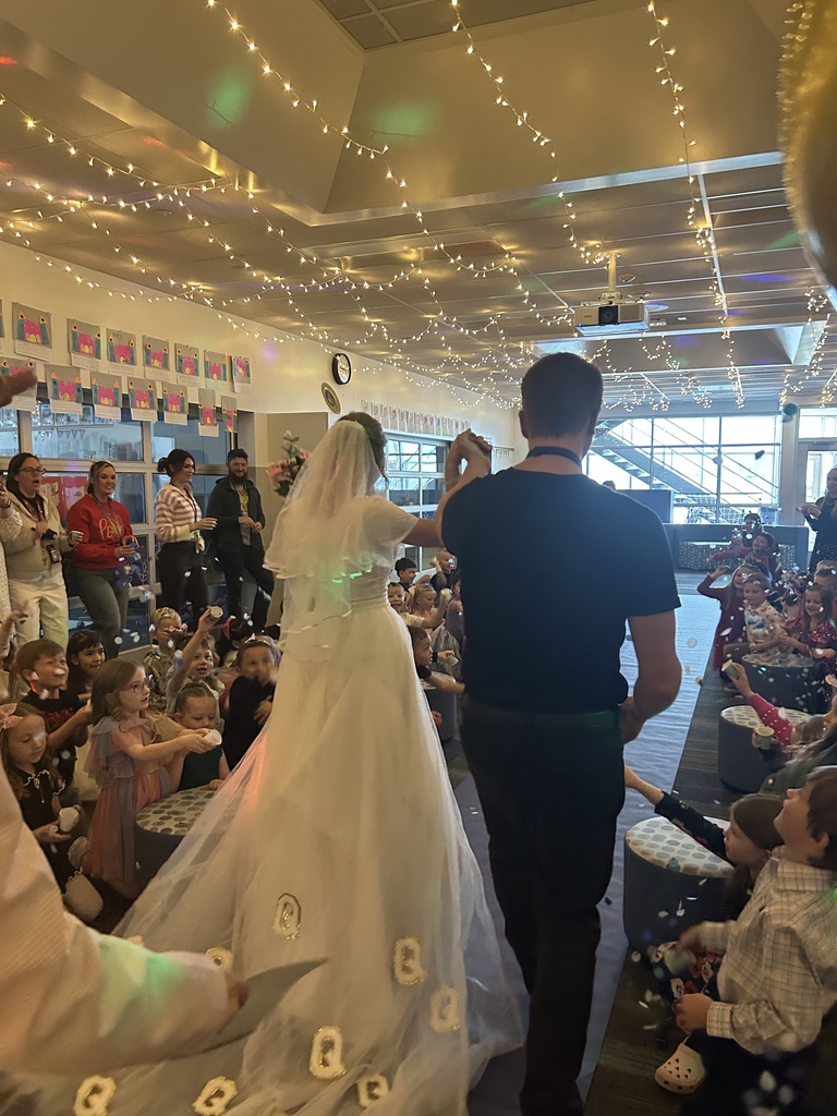 women with brides gown and Q's on it walking in middle of group of students throwing confetti