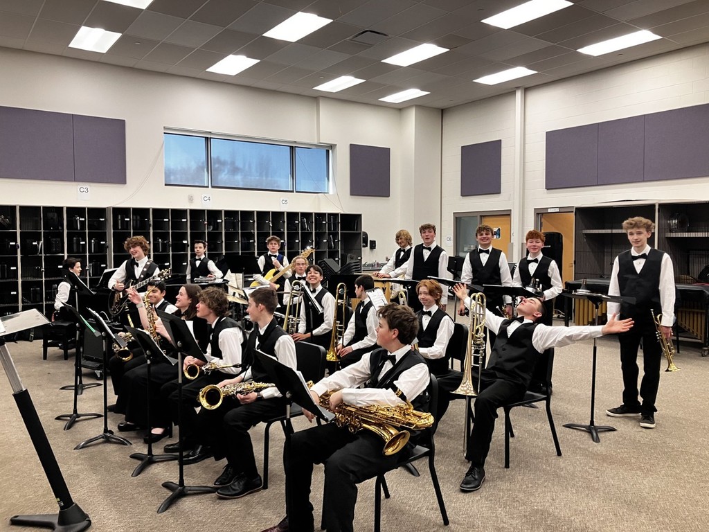 19 students dressed in long, white sleeved shrits and black bow ties, vests, and pants with their instruments. Most students are sitting, while some are standing as they get warmed up for the State Jazz Band festival.