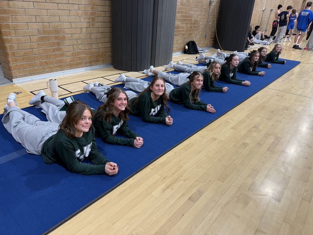 Cheerleaders supporting the wrestling team, lying down on a mat. 
