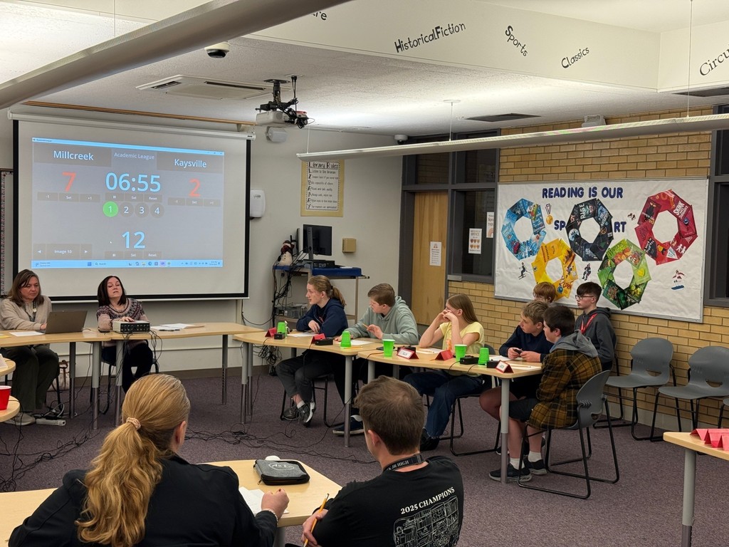 image of students sitting at desks with a screen behind them