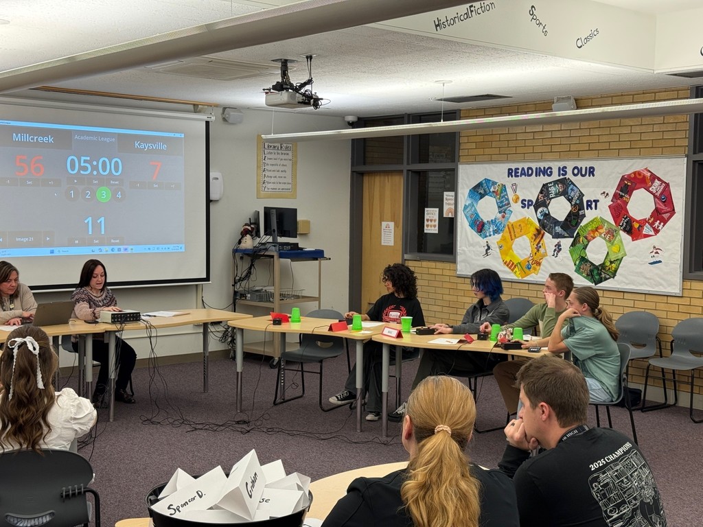 image of students sitting at desks with a screen behind them
