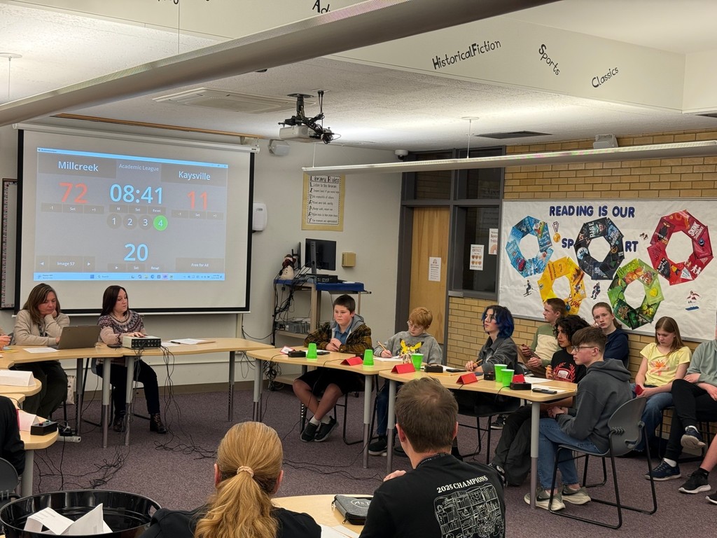 image of students sitting at desks with a screen behind them