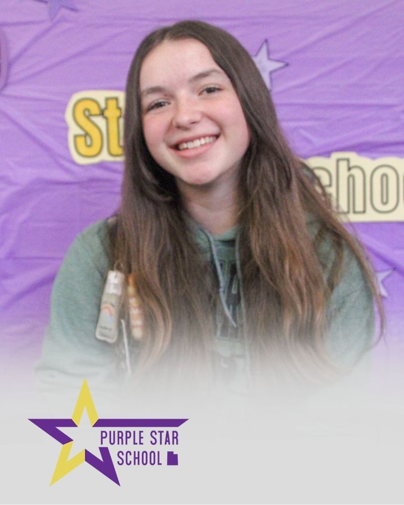 A student sitting in front of a banner that says Purple Star School 