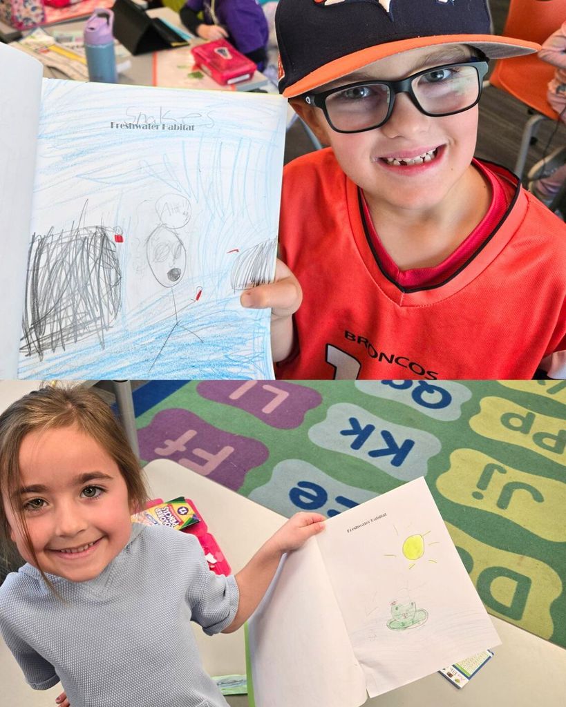 Students proudly hold up their freshwater habitat journal pages featuring colorful drawings of animals and environments.