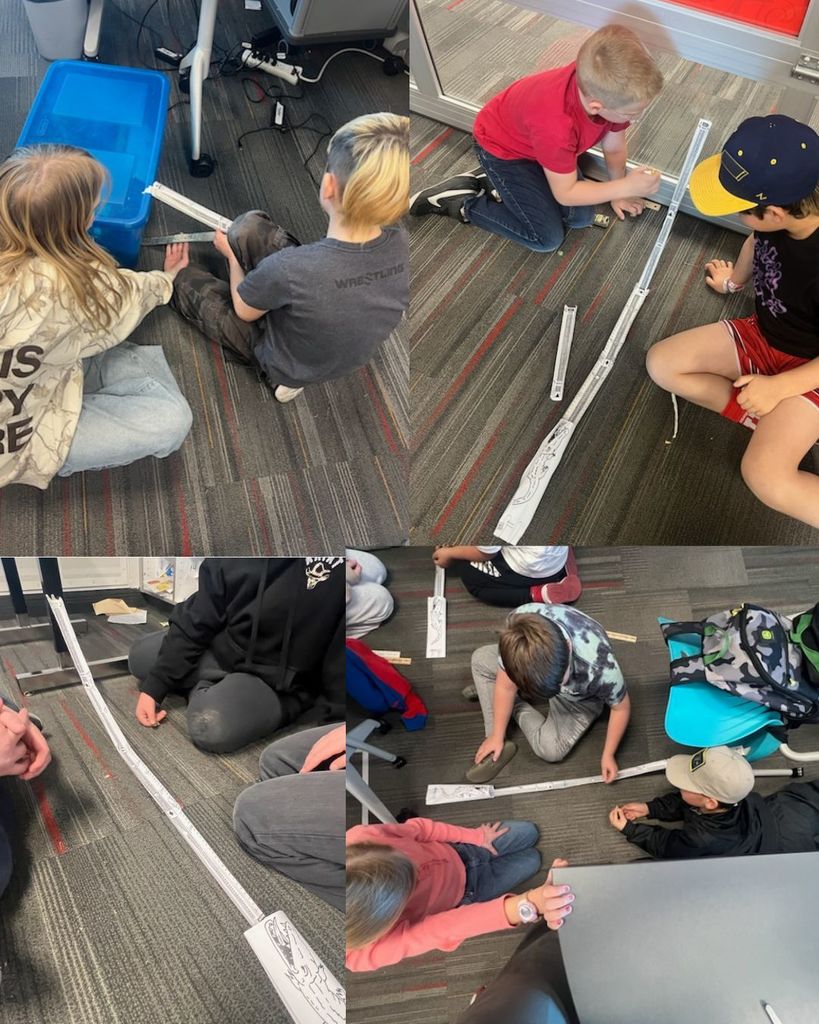 Students sit on the classroom floor working together to build paper roller coaster tracks. They test marbles on the tracks to explore how height and motion affect speed and movement.