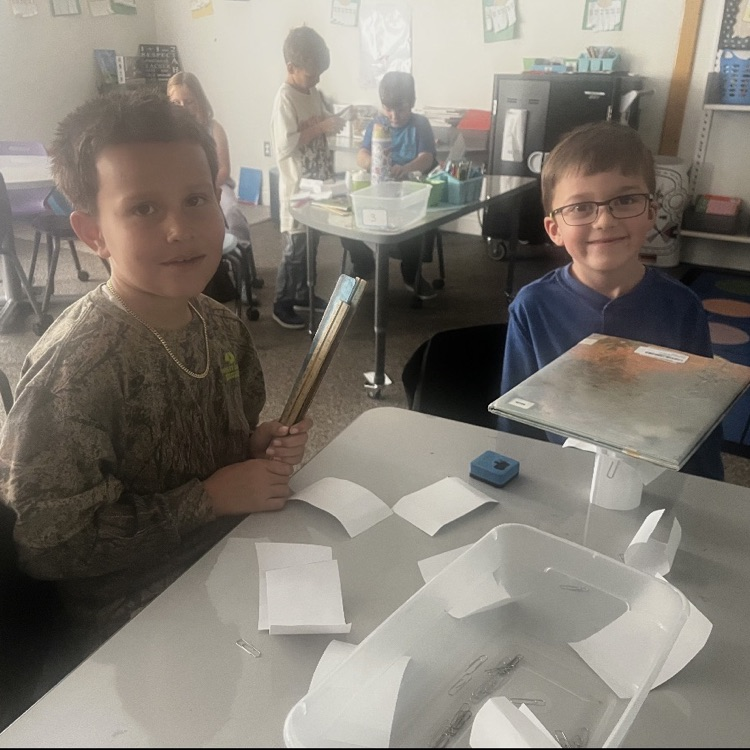 two boys using papers to hold up a book