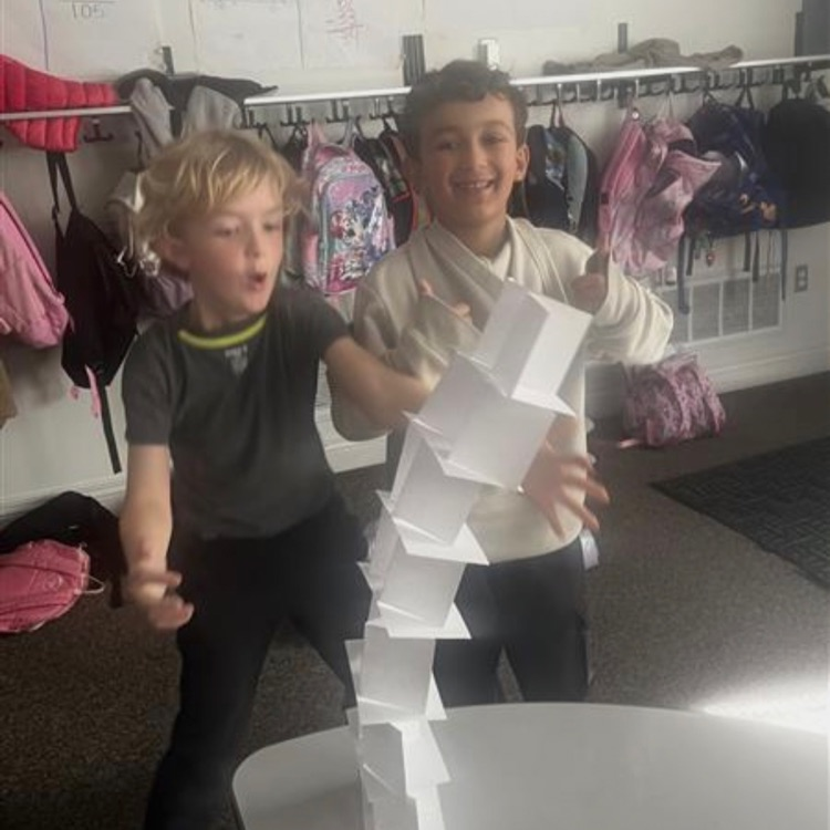 boys building a paper tower and it is leaning 