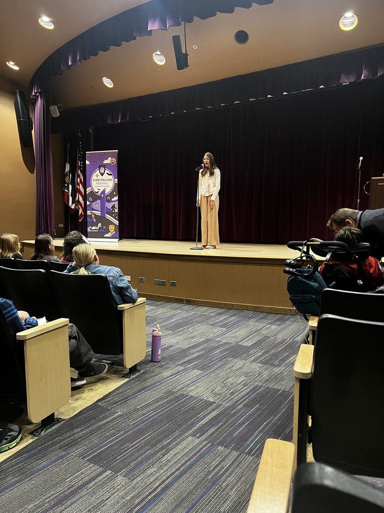 image of student standing on stage speaking in a microphone with people in the audience